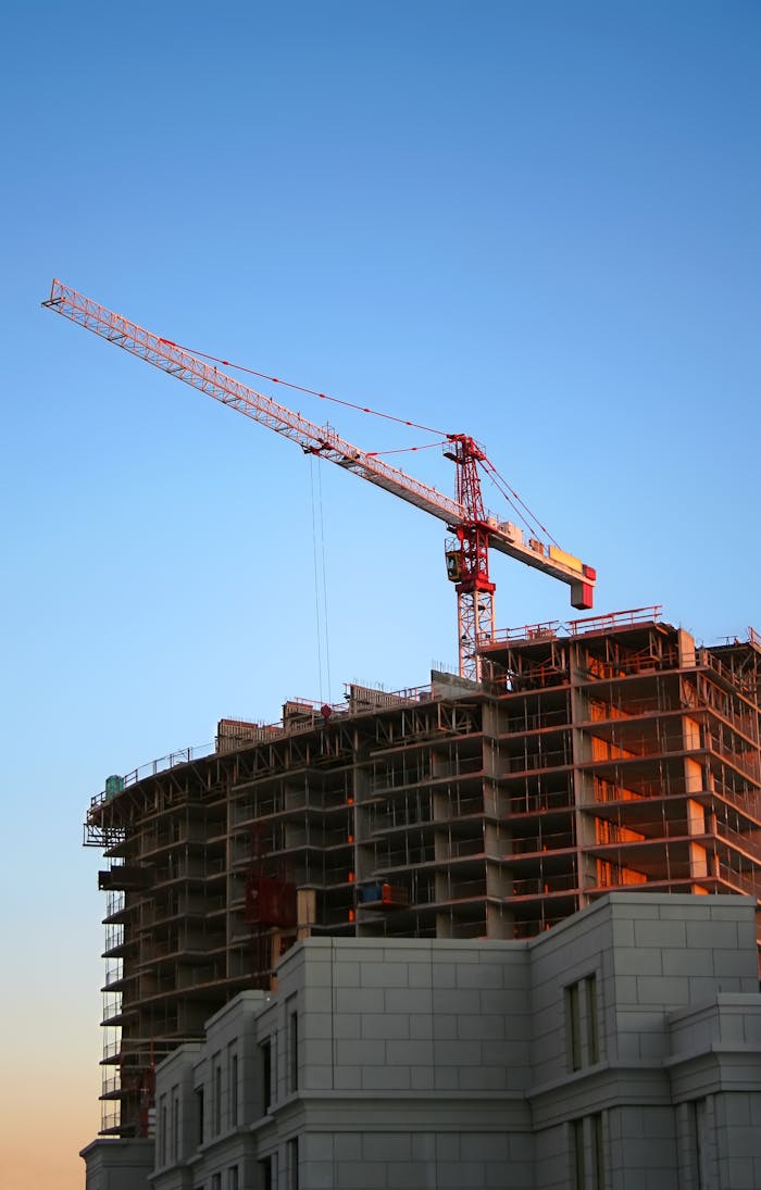 who-we-are Tower crane on a high-rise building under construction at sunset, showcasing modern urban development.
